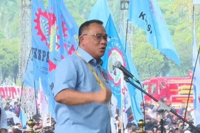 Menteri Lingkungan Hidup/Kepala Badan Pengendalian Lingkungan Hidup (KLH/BPLH) Moh Jumhur Hidayat menyampaikan orasi di hadapan massa dengan latar bendera organisasi buruh dan peserta aksi yang memadati lokasi kegiatan.