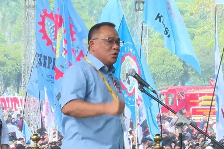 Menteri Lingkungan Hidup/Kepala Badan Pengendalian Lingkungan Hidup (KLH/BPLH) Moh Jumhur Hidayat menyampaikan orasi di hadapan massa dengan latar bendera organisasi buruh dan peserta aksi yang memadati lokasi kegiatan.